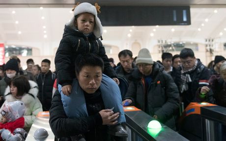 Asian father holding son on shoulders, going through a turnstile, Asian men behind him