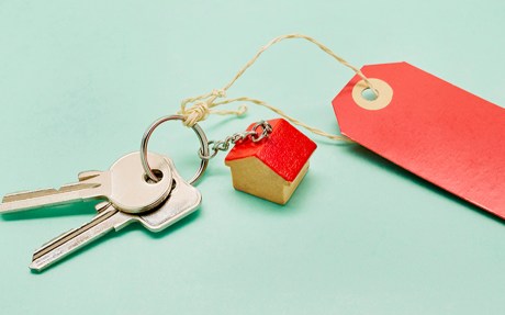 Still life of a keyring with keys, a small house and red price tag on turquoise colored background