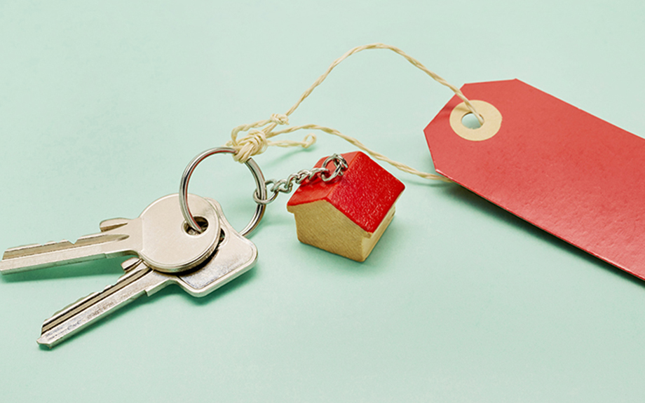 Photo: Still life of a keyring with keys, a small house and red price tag on turquoise colored background