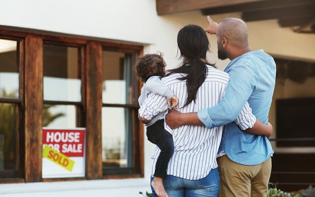 Photo: young ethnic family looking at a home with house of sale sign and sold over it.