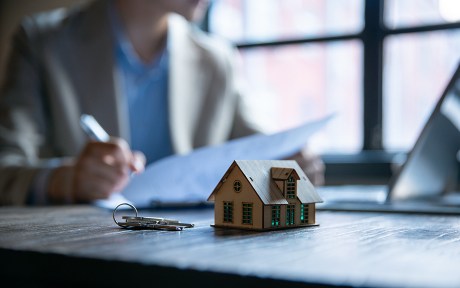 photo: person signing papers with model house and keys on the table near them.