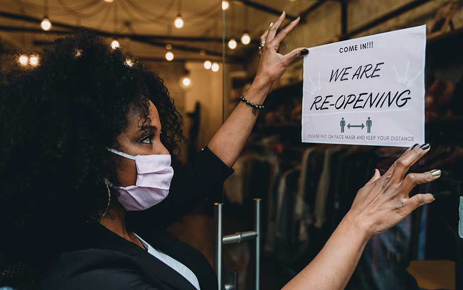 Photo: African American woman business owner with COVID mask putting up sign for business reopening