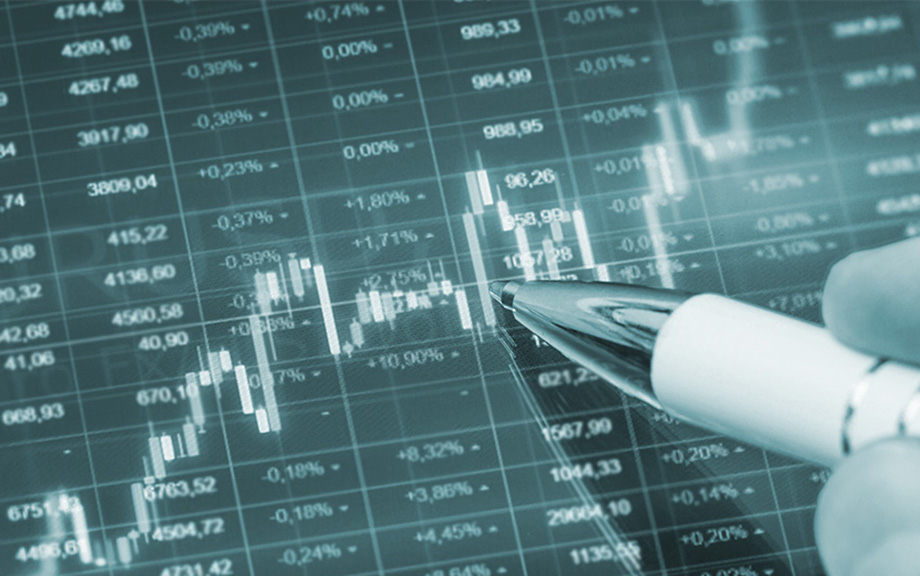 Decorative photo: digital terminal screen with rows and columns of numbers and candlestick chart over it with hand with a pen pointing on the chart.