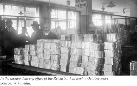 Photo: In the money delivery office of the Reichsbank in Berlin: table full of money notes with men looking over. Sign says Rauchen verboten, October 1923; source: Wikimedia.