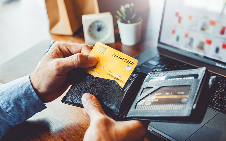 Decorative photo: man's hand pulling out a yellow credit card from a wallet with several other credit cards.