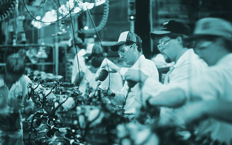Decorative image: Factory workers on an assembly line with baseball caps on.