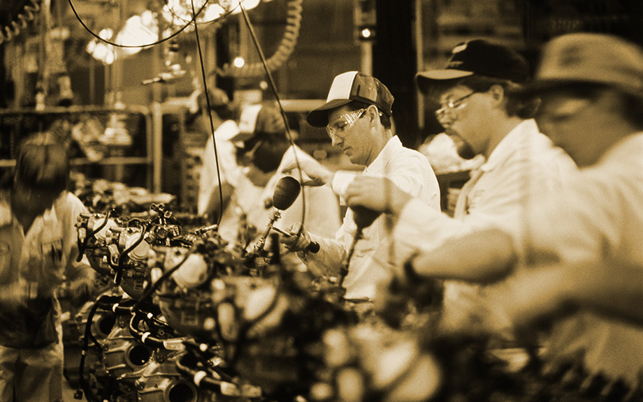 Decorative image: Factory workers on an assembly line with baseball caps on.