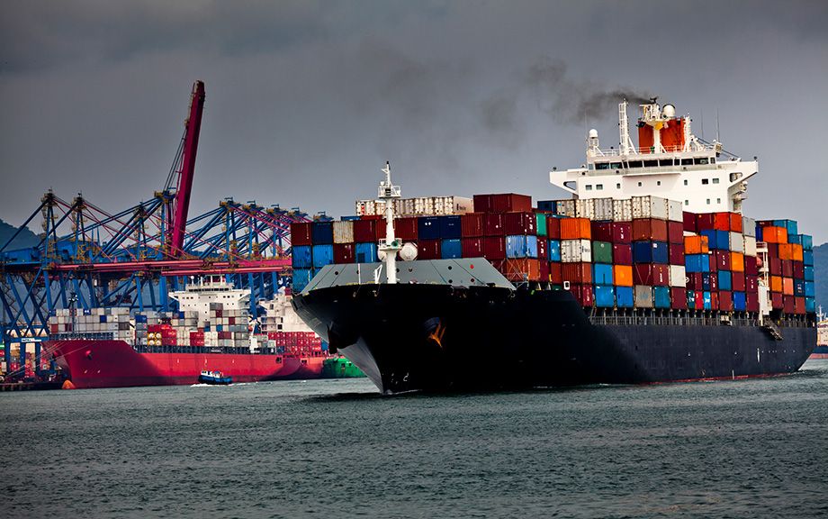 decorative photo of several cargo ships in a harbor. One is moving out of port.