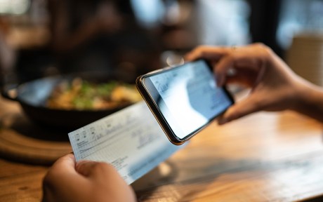  Man depositing check by phone while sitting at a table in a restaurant