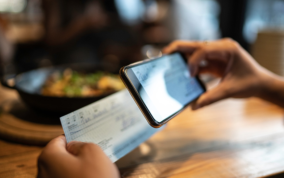 Photo: Man depositing check by phone while sitting at a table in a restaurant