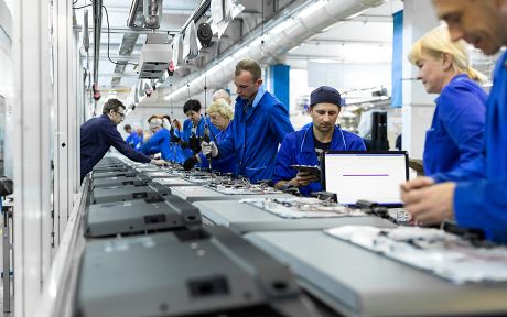 Photo: assembly line with several men and women in blue overalls.