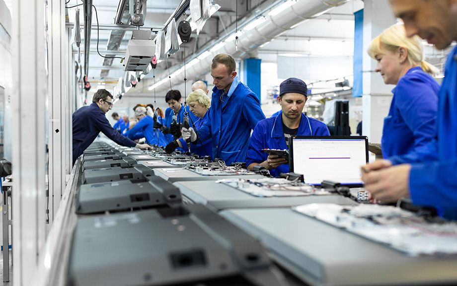 Photo: assembly line with several men and women in blue overalls.