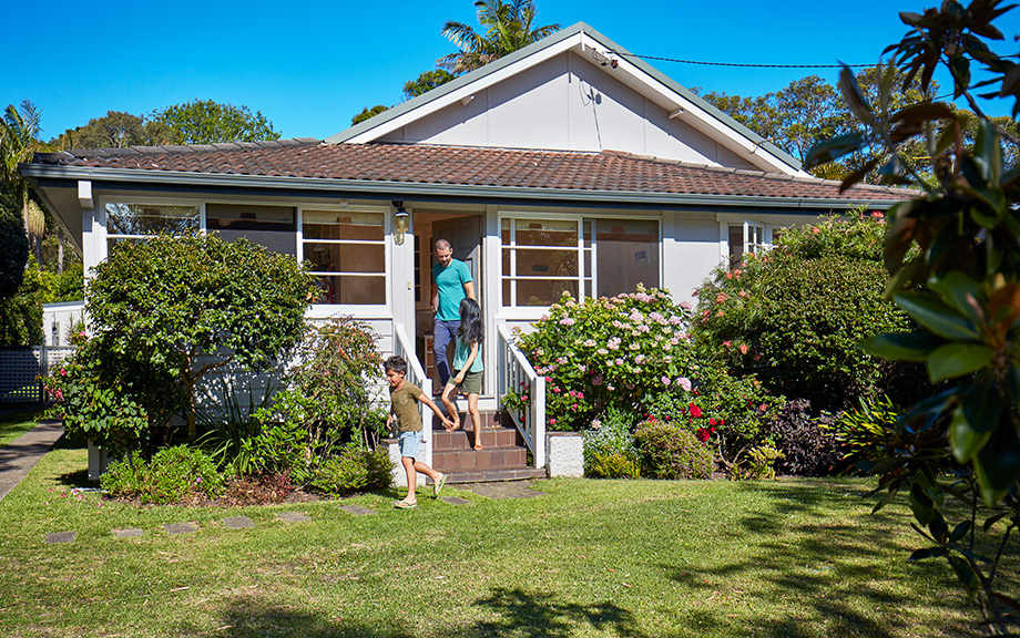 Decorative Image: Boy and parents coming out of house. Family is spending leisure time in yard. Plants growing in lawn on sunny day.