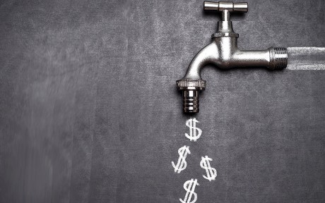 Decorative photo of silver spigot on blackboard with dollar signs chalked on the board coming out of the spigot.