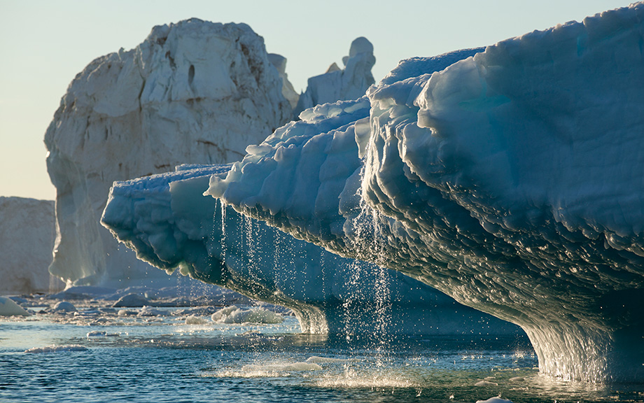 Photo of a melting iceberg with water trickling down splashing into a water body.