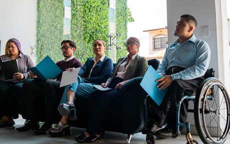 Group of people waiting for job interview in the waiting room at office - including young wheelchair user