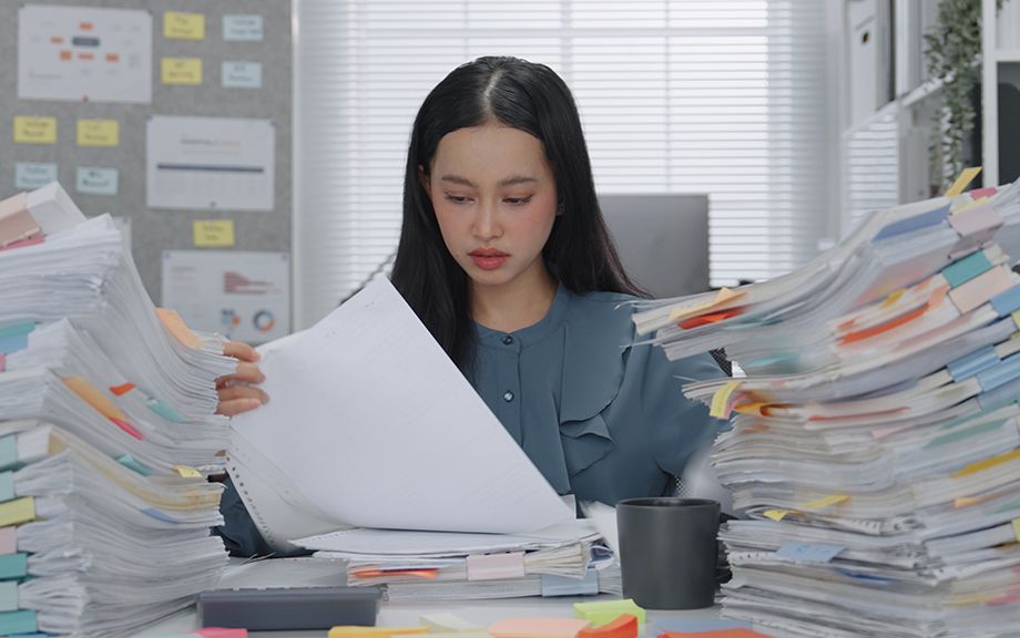 Asian Business woman working busy with massive stacks of documents check and review preparation data report or organizing paperwork workplace stress and administrative overload