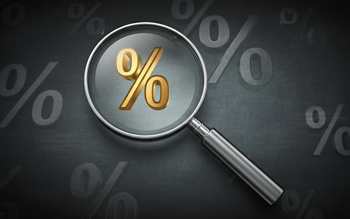Image of an interest rate sign with a magnifying glass hovering over it. Black and gray background with interest rates in gray on it.