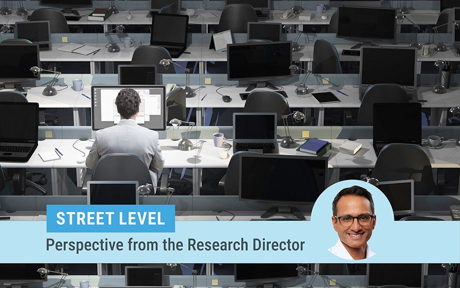 Street level column by Research Director Kartik Athreya. Image of Athreya on top of a photo of a large room with rows of desks and laptops with only one man sitting at one desk working.